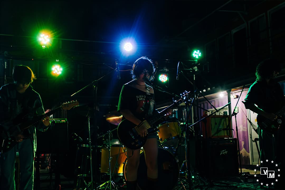 ZZK sobre el escenario bajo luces verdes y azules, con guitarras al frente y batería al fondo.
